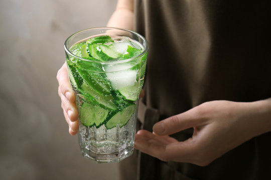 Young woman holding glass of delicious refreshing water with mint and cucumber, closeup