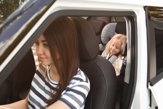 Young woman driving car with small girl in safety seat