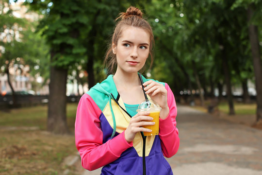 Young woman walking outdoors with yellow smoothie