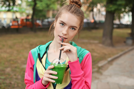 Young woman walking outdoors while drinking green smoothie