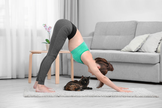 Young Beautiful Woman With Cat Practicing Yoga Pose At Home