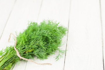 Heap of green fresh raw dill tied of brown rope on old wooden white rustic planks