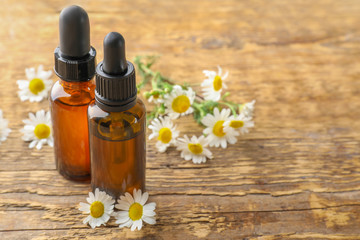 Bottles of essential oil and chamomile flowers on table