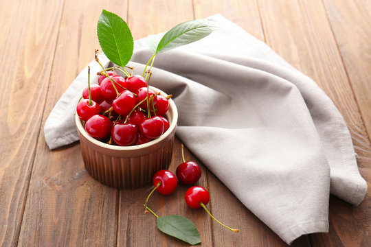 Ripe cherries in bowl with napkin on wooden background