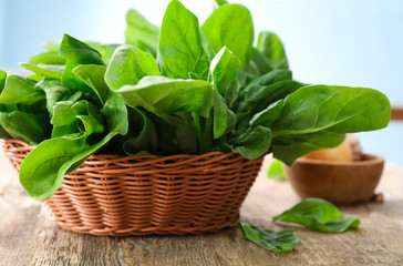 Wicker basket with fresh spinach leaves on table