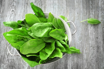 Colander with fresh spinach leaves on table