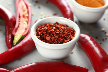 Red chili flakes and pepper pods on grey background