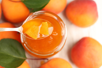 Apricot homemade jam in jar with spoon and ripe juicy fruit on table