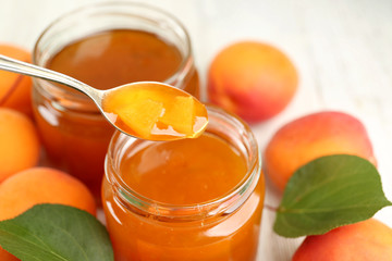 Apricot jam in jars with spoon and ripe juicy fruit on table