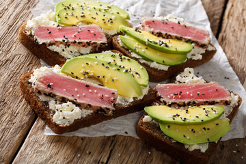 Super food: sandwiches with tuna steak in sesame, avocado and cottage cheese close-up. vertical