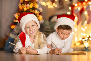 Cute kids writing letter to Santa in room decorated for Christmas