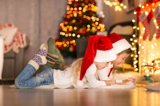 Cute Kids Writing Letter To Santa In Room Decorated For Christmas