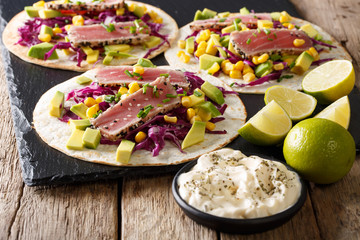 Naklejka na ściany i meble Fish takos with fried tuna, corn, red cabbage, lime and avocado close-up. horizontal