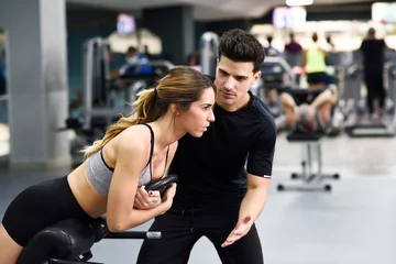 Tuinposter Personal trainer helping young woman lift weights © javiindy