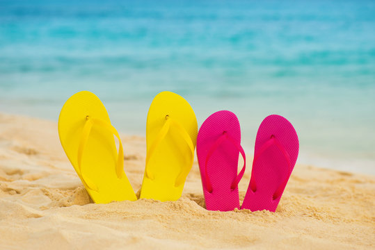 Yellow and pink sandals stand in the sand against the background of the sea.