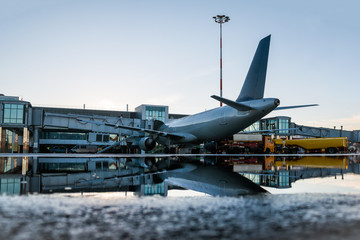 Ground handling of a passenger airplane parked to a jet bridge with reflection in a puddle