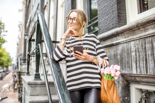 Portrait of a young elegant woman with smart phone standing on the stairscase of a luxury residential house in Amsterdam