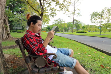 Portrait of young hipster man  reading a book on the bench in beautiful outdoor park. Wide angle shot