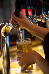 barman stuffs glass of beer from keg in  bar. vertical image