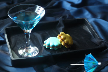 Two Seashell Macarons on black tray and Blue Cocktail in martini glass, on dark background. - Powered by Adobe