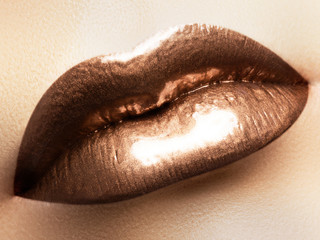 Cosmetics and make-up. Shoot of a beautiful girl with golden lips lipstick and gloss. Sexy and stylish lips. Lips against the backdrop of smooth skin. Fashion golden lips closeup located diagonally