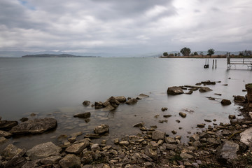 Long exposure photo of rocks and stones in a lake, with perfectly still water and overcast sky