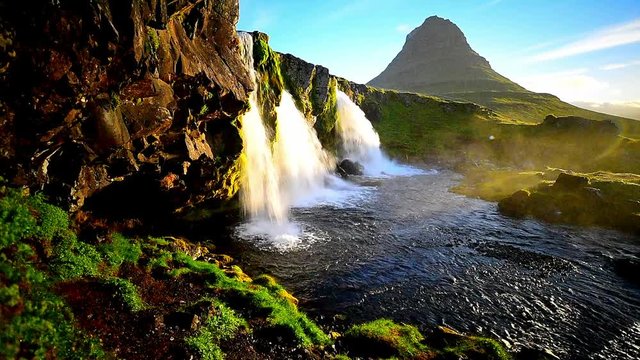 mt. Kirkjufell with Amazing Waterfall with Green Grass and Blue Sky. Powerful Water Flow.