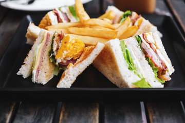 Slices sandwiches with french fried, on black dish, on wooden table