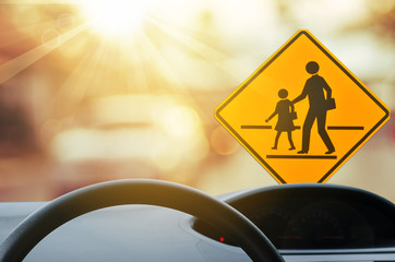School zone warning sign and inside car view ,steering wheel on blur traffic road with colorful...