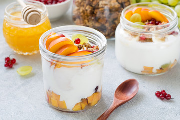 Greek yogurt, fresh fruits, honey and granola breakfast in jar. Bright morning healthy eating or dieting concept. Closeup view, horizontal composition