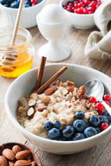 Oatmeal porridge with blueberries, almonds, cinnamon, honey, linseeds and red currants in bowl. Super food for healthy nutritious breakfast
