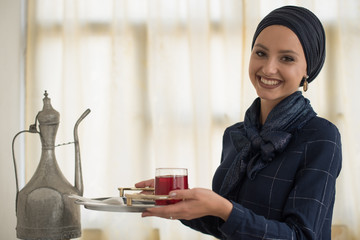 happy young woman wearing hijab holding plate with baklava and glass full of juice 