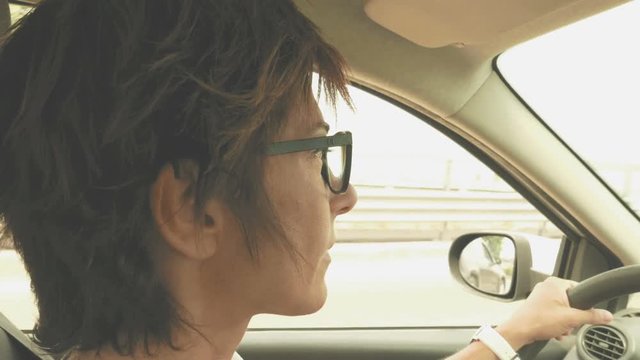 Woman with eyeglasses driving car with hands on steering wheel. Interior close up, side view, traffic on street. Vintage filter, toned image.