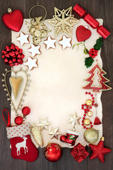 Christmas festive background border with bauble decorations, holly, mistletoe, gingerbread biscuits on parchment paper on oak wood.