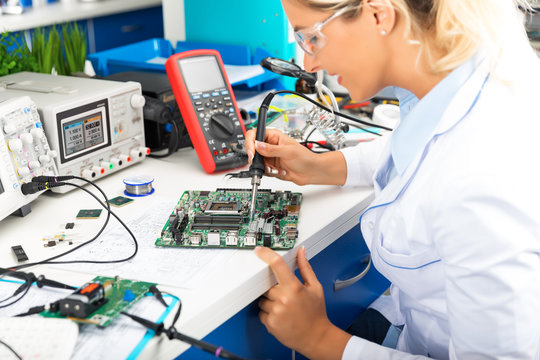 Young female electronic engineer soldering computer motherboard in laboratory
