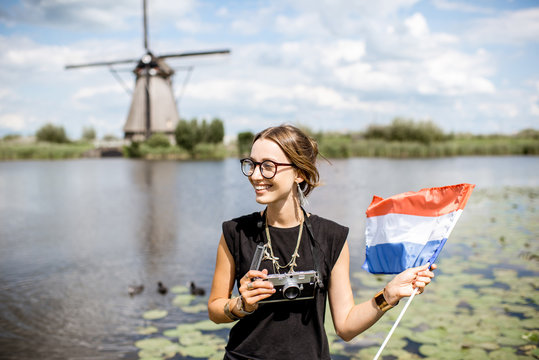 Portrait of a young woman tourist standing with dutch flag on the beautiful landscape background with old windmills in Netherlands