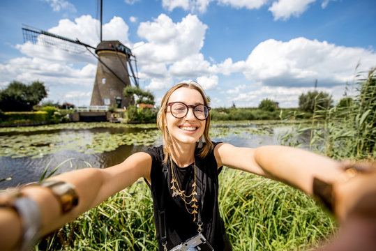 Young woman tourist making selfie photo on the beautiful landscape background with old windmills in Netherlands