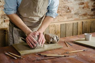 pottery, clay, ceramics art concept - closeup on hands of young master with the large pieces of fireclay