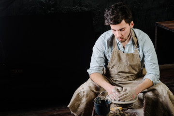 pottery, workshop, ceramics art concept - man working on potter's wheel with raw clay with hands, a...