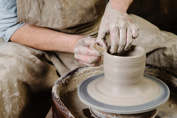pottery, workshop, ceramics art concept - closeup on male hands sculpt new utensil with a tools and water, man's fingers work with potter wheel and raw fireclay, front close view
