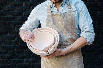 potter, utensils, ceramics art concept - smiling male ceramist in the apron shows samples of clay...