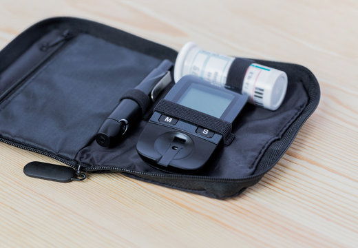 Glucometer, lanset and test strip lies in bag case  on the wooden table on the left side. Concept of health, medicine. Macro