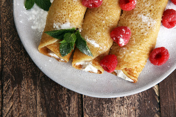 Homemade crepes served with fresh raspberrries and powdered sugar on rustic wooden table