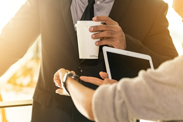 Closed up of businessman with take away coffee in hand while businesswoman looking at wristwatch and holding tablet in her hands