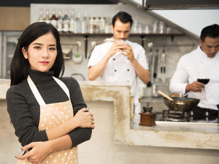 portrait of Young Beautiful woman cooking healthy food in the kitchen.She arms crossed and smile , background is two male chefs are cooking .