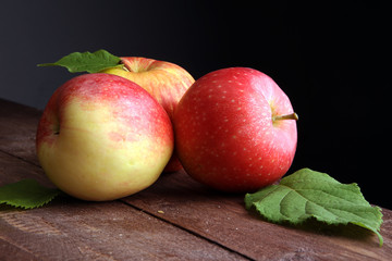 Ripe red apples with leaves on wooden background
