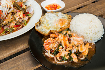 Rice topped with stir-fried combination of pork, chicken, squid, shrimp, basil and fried egg. Thai food. (Focus on fried basil and shallow depth of field)