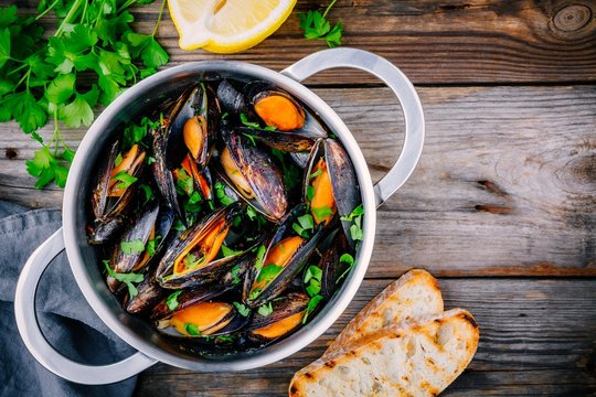Delicious seafood mussels with with sauce and parsley.  Lemon and baguette . Clams in the shells.