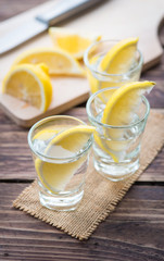 Vodka with lemon in shot glass on wooden background