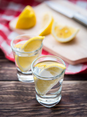 Vodka with lemon in shot glass on wooden background